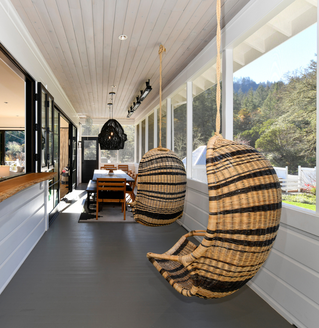 Luxurious enclosed porch of a Calistoga Valley vacation rental, featuring elegant hanging rattan chairs and scenic views of surrounding trees.